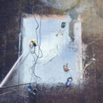 Top view of workers cleaning a large surface with equipment and water hoses. - Photo by Saruhan Osmanoğlu on Pexels