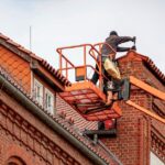 Roofer in a cherry picker conducting maintenance on a red brick building with a tiled roof. - Photo by Gundula Vogel on Pexels