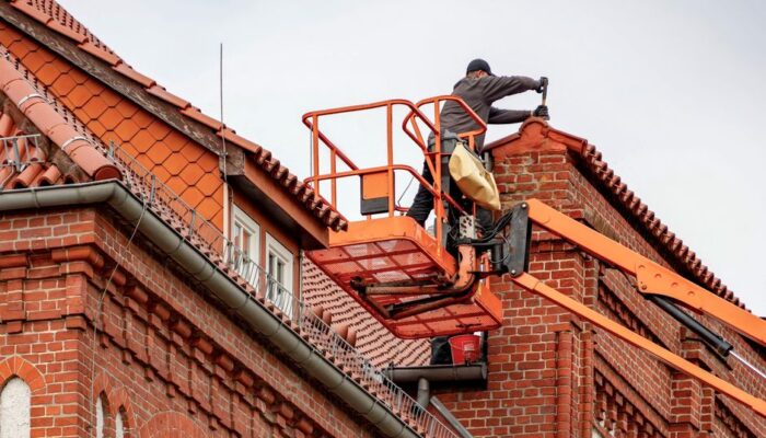 Roofer in a cherry picker conducting maintenance on a red brick building with a tiled roof. - Photo by Gundula Vogel on Pexels